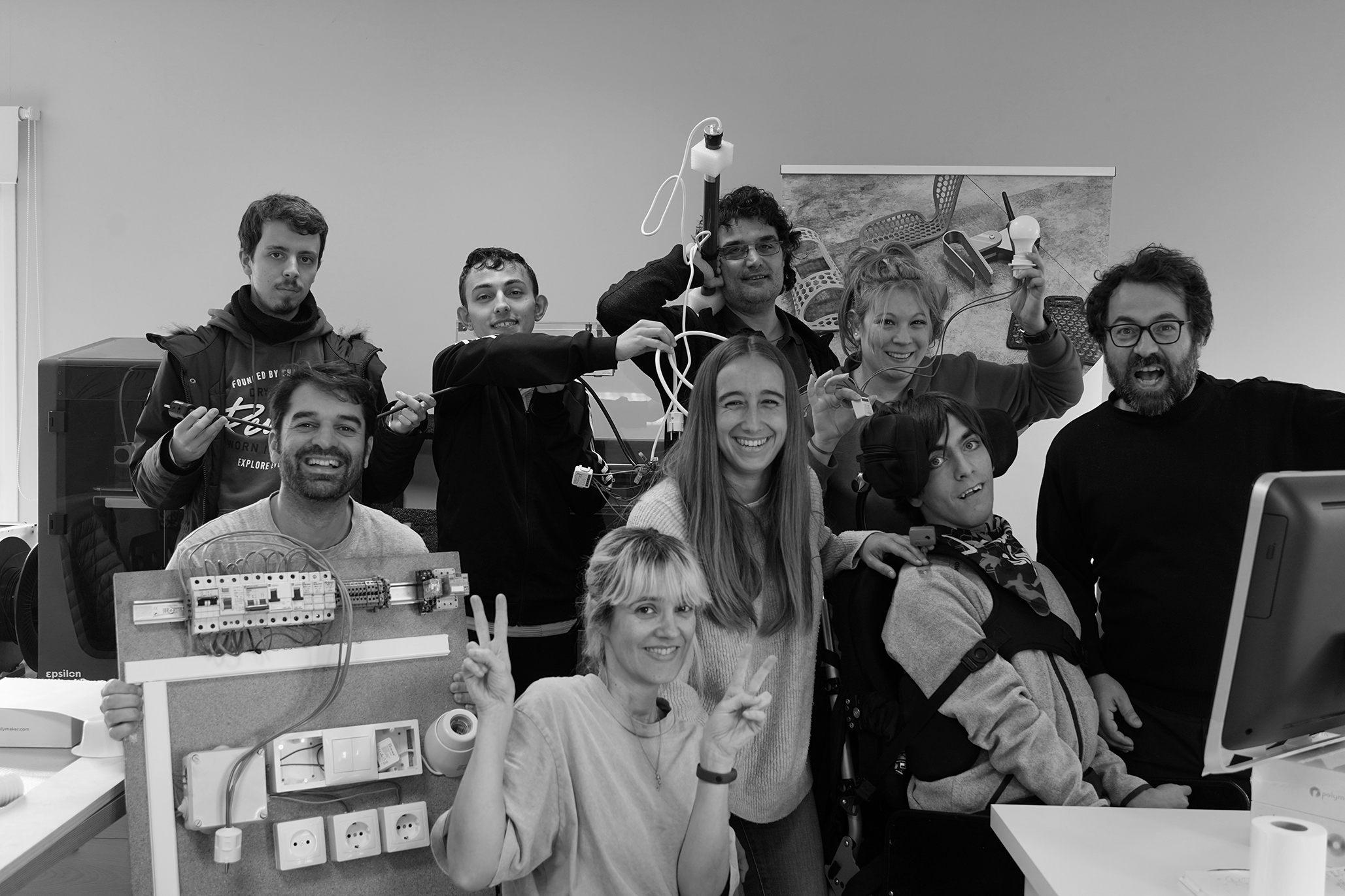 Grupo de personas con y sin discapacidad, en la oficina de 3DLAN posando para una fotografía sujetando aparatos electrónicos.