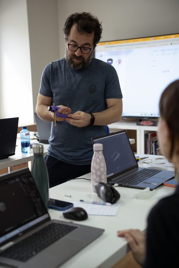profesor enseñando una pieza impresa en 3D a alumnos con ordenadores