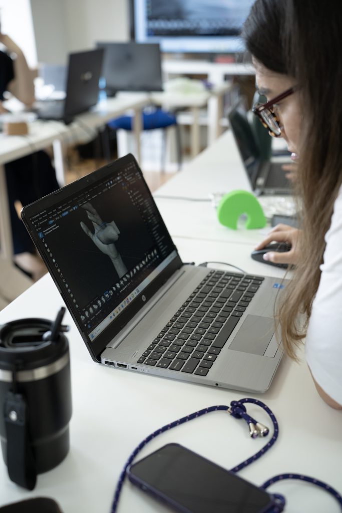 Persona utilizando un ordenador portátil con un software de modelado 3D que muestra una mano en pantalla, mientras maneja un ratón.