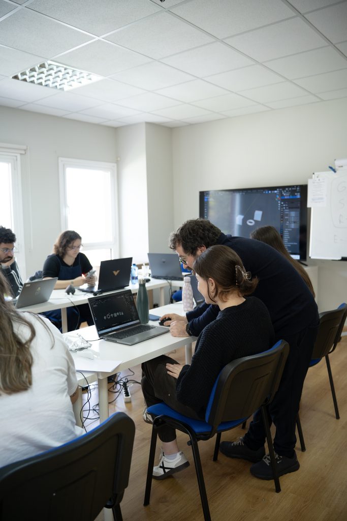 persona enseñando a alumnado sentados en mesas con ordenadores y programas de diseño en las pantallas