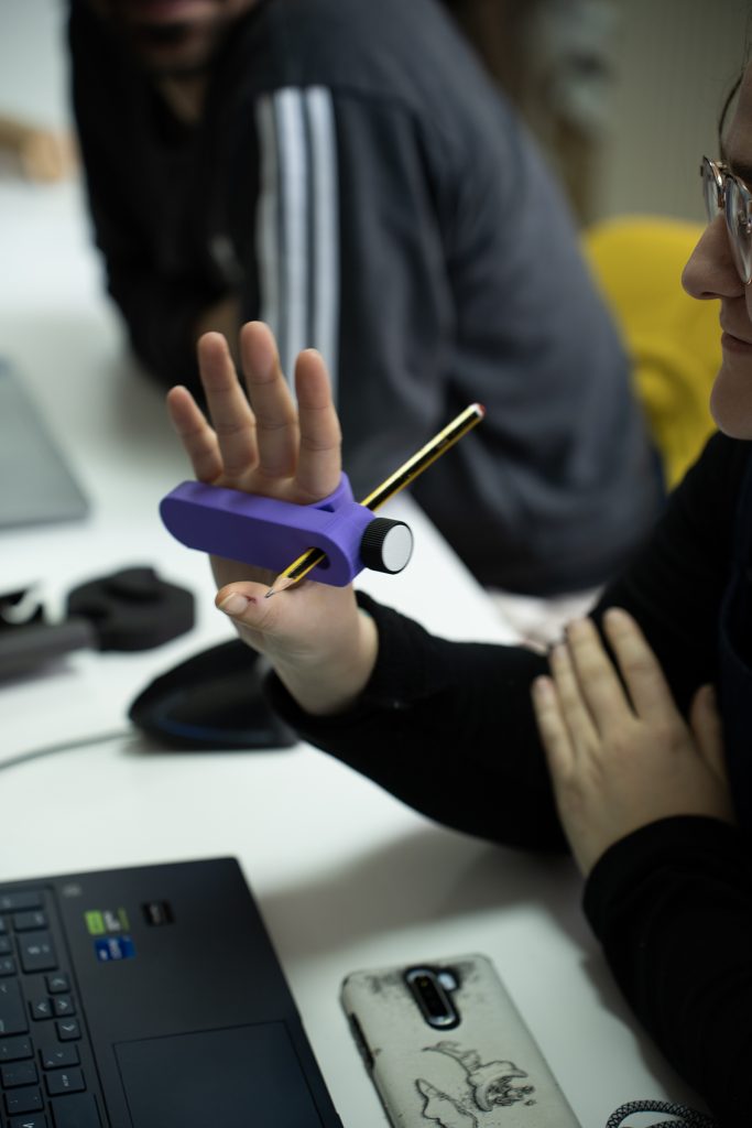 una mano sujeta un producto de apoyo para sujetar lápices impreso en 3D de color morado