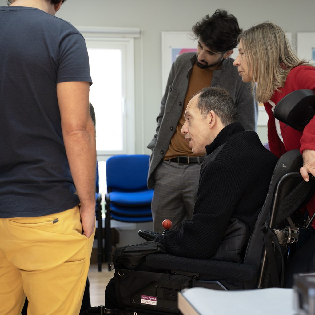 Grupo de personas reunidas alrededor de una persona en silla de ruedas, observando algo que está fuera de imagen.