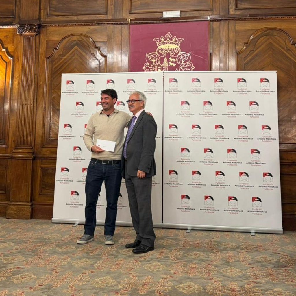 Una persona entrega a otra un premio delante de un panel lleno de logotipos.