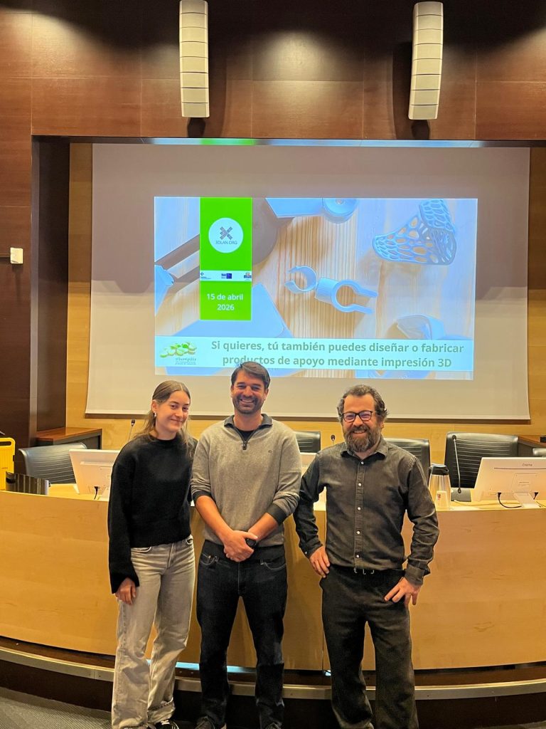 Tres personas trabajadoras de 3DLAN posan delante de un escenario con una pantalla que proyecta la web de 3dlan.org