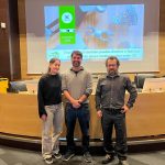 Tres personas posan delante de un escenario con una pantalla que proyecta la web de 3dlan.org