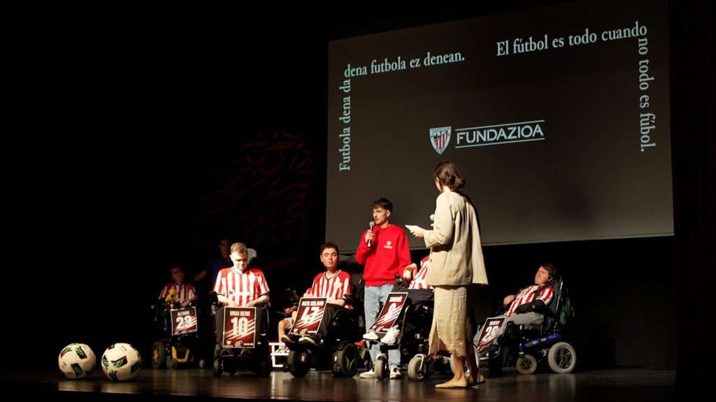 Jóvenes con camiseta rojiblanca en silla de ruedas eléctrica durante la presentación.